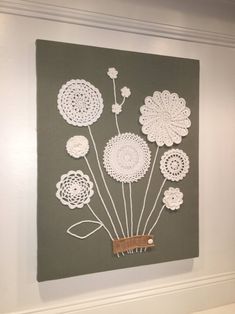 a wall hanging with crochet flowers on it in a white walled room next to a gray wall