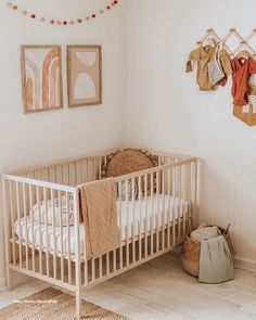 a baby crib in a room with pictures on the wall and clothes hanging up