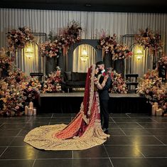 a bride and groom standing in front of a decorated stage at their wedding reception with floral arrangements