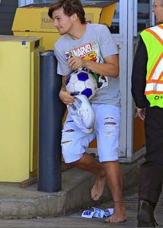 a man holding a soccer ball while walking down the street with another man in front of him