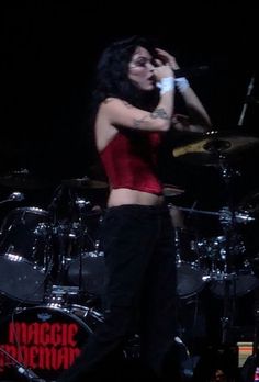 a woman in red shirt and black pants on stage with drum set next to her