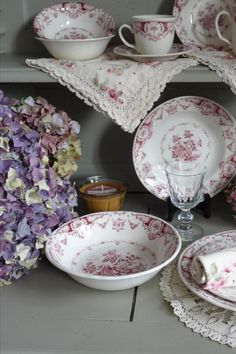 an assortment of pink and white china on display with purple flowers in the foreground