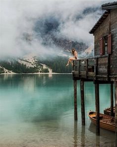 a woman is sitting on a dock in front of a mountain lake with a boat