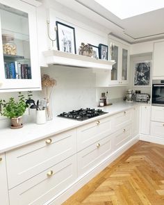 a kitchen with white cabinets and wood floors is pictured in this image, there are plants on the counter