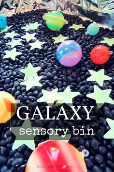 some balloons and stars are in the middle of black beans with text overlay that reads galaxy sensory bin