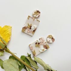 two pieces of ceramic with flowers on them next to a yellow flower and green leaves