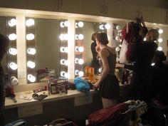 a woman standing in front of a mirror looking at her hair and make - up