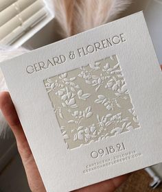 a person holding up a card that says gerard & horrece on it with feathers in the background