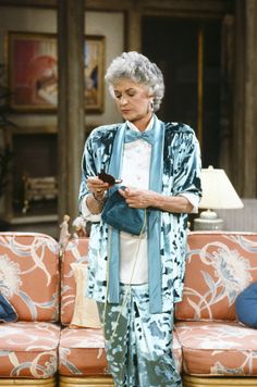 an older woman standing in front of a couch looking at her cell phone