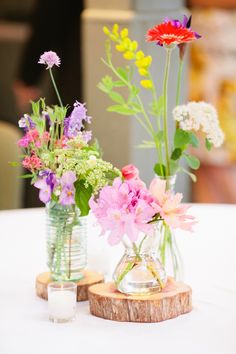 two vases filled with flowers sitting on top of a white table covered in wood slices