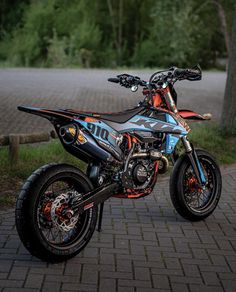 a dirt bike parked next to a tree on a brick road in front of some trees