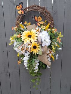 a wreath with sunflowers, daisies and other flowers hanging on a fence