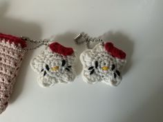 two hello kitty crocheted keychains hanging from chains on a white surface