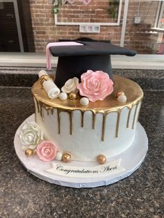 a cake decorated with flowers and graduation cap on top of a marble countertop in front of a brick wall