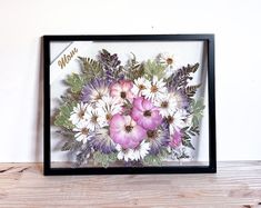 a black frame with flowers in it sitting on a wooden table next to a white wall