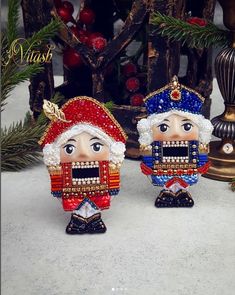 two figurines sitting next to each other near a christmas tree with ornaments in the background