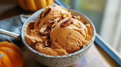 a bowl filled with ice cream and pecans on top of a table next to pumpkins