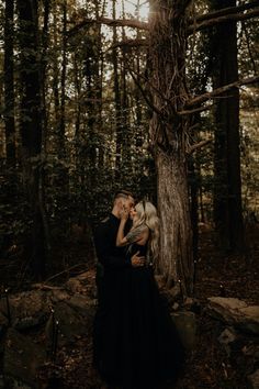 a man and woman standing next to each other near a tree in the middle of a forest