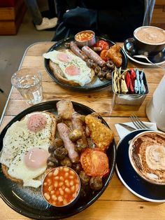 two plates with breakfast foods on them sitting on a table next to cups of coffee