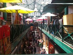 people are walking through an indoor market with umbrellas overhead and tables in the middle