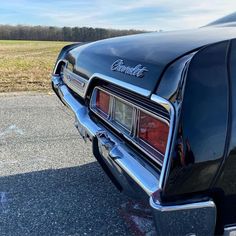 the front end of an old car parked in a parking lot with grass and trees behind it