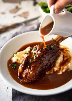 someone pouring gravy on top of mashed potatoes in a white bowl with meat