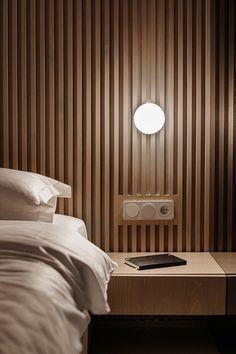 a bed with white sheets and pillows next to a night stand on top of a wooden table