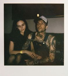 a man and woman sitting next to each other with tattoos on their arms, looking at the camera