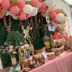 a table topped with lots of desserts and balloons in front of a wall filled with greenery