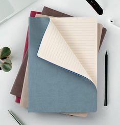 several notebooks and pens on a white table with a computer keyboard, pen and plant