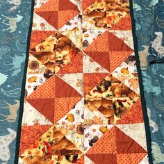 an orange and white quilt is laying on a blue tablecloth with flowers in it