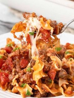 a fork full of pasta with meat and tomato sauce on it, being lifted from a white plate