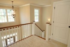 an empty room with white stairs and light fixture on the wall, next to two windows