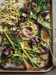 a tray filled with noodles, broccoli and other vegetables next to spoons