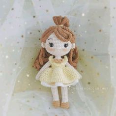 a crocheted doll is wearing a yellow dress and standing on a white sheet