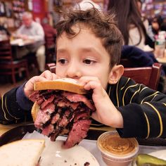 a young boy eating a large sandwich in a restaurant