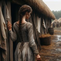 a woman standing next to a hut with straw bales on the roof and walls