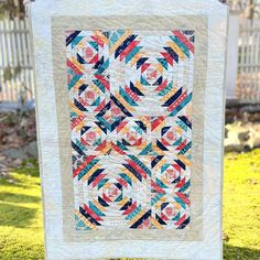 a quilt hanging from a clothes line on the grass in front of a white fence