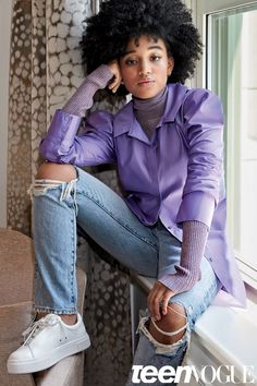 a woman sitting on a window sill with her legs crossed and wearing ripped jeans