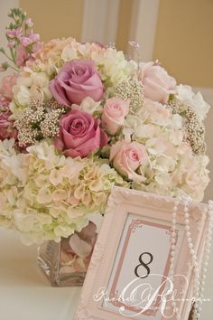 a vase filled with pink and white flowers next to a table number sign that reads 8 o'clock