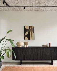 a living room with a large plant in the corner and a painting on the wall