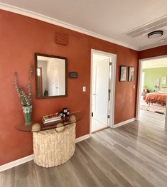 a living room with orange walls and wood flooring in the center is an entry way that leads to a bedroom