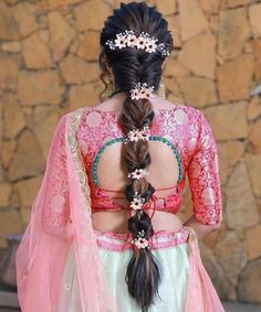 a woman with long hair wearing a pink and white dress standing in front of a stone wall