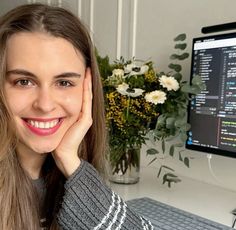 a woman sitting in front of a computer with her hand on her chin and smiling