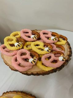 there are many pretzels on the wooden platter that is decorated with pink and yellow icing