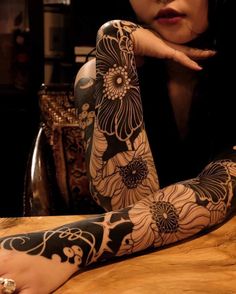 a woman sitting at a table with tattoos on her arms