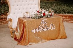 the table is set up with gold sequins and white chairs for guests to sit on