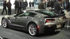 a silver car is on display at an auto show with people walking around the area