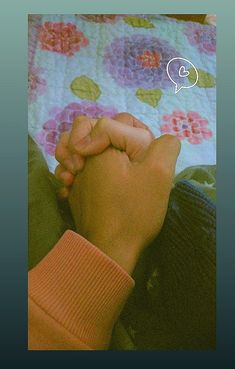 two people holding hands on top of a bed with a flowered comforter behind them