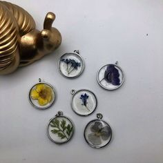 six pendants with pressed flowers on them sitting next to a teapot ornament